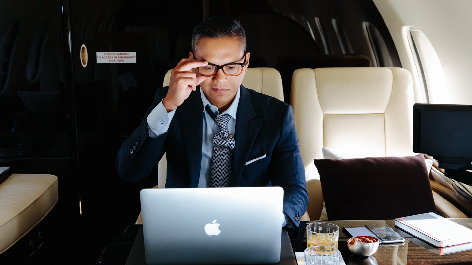 Man adjusting glasses while looking at laptop screen in a business jet