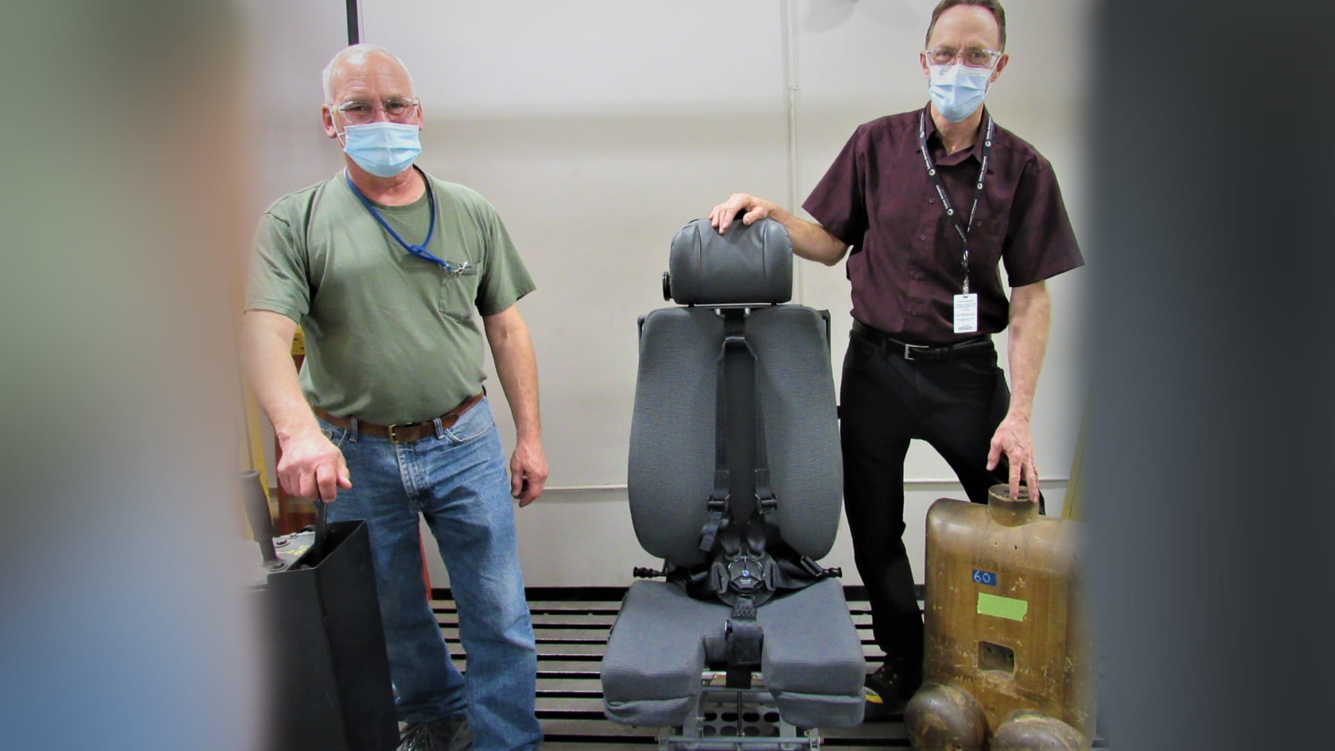 Shawn (right) and assembler Frank Mimlitsch pose with a pilot seat in a Colorado Springs test lab.