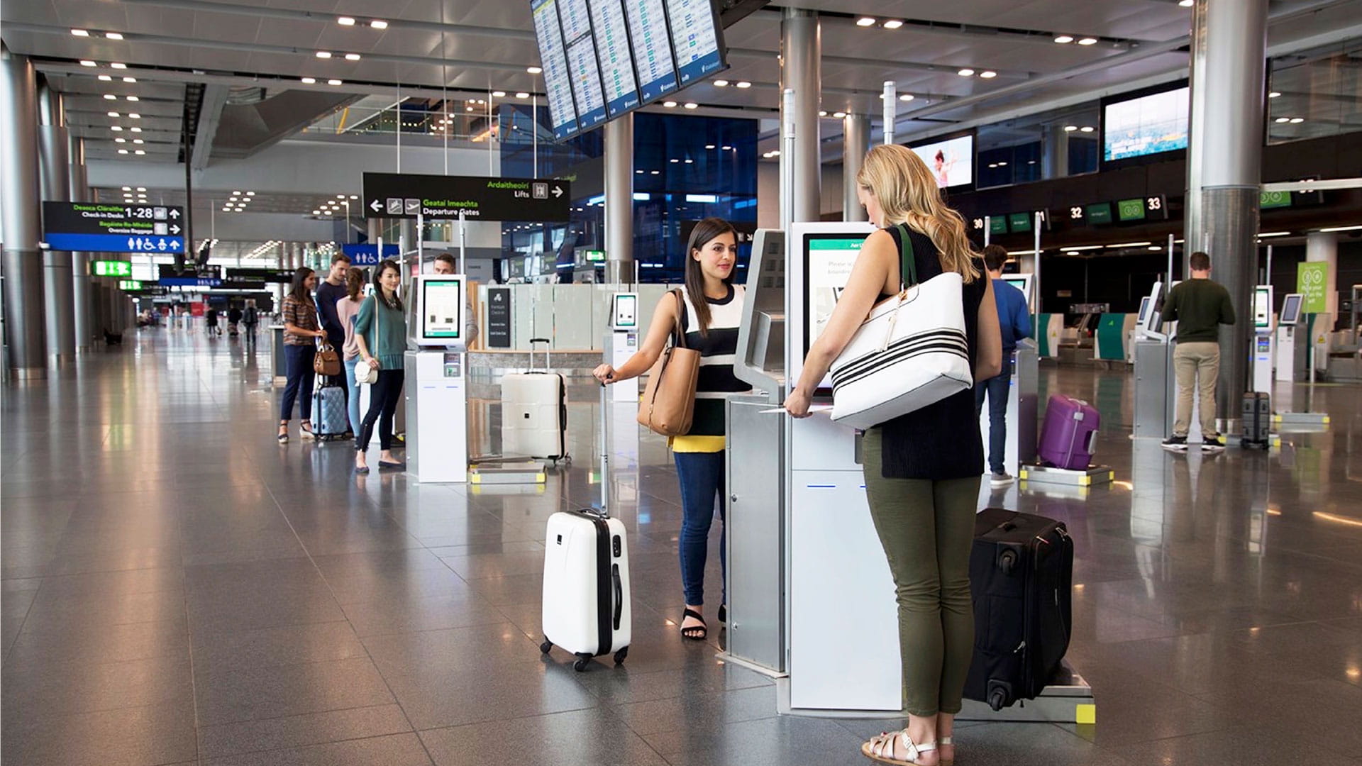 Two women using airport kiosks