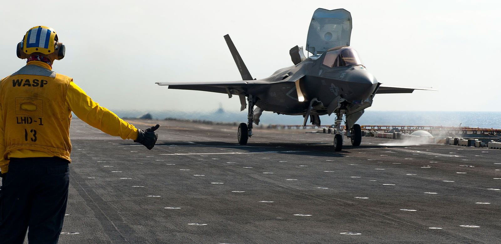 Jet landing on the deck of a ship with a crewman giving the thumbs up.