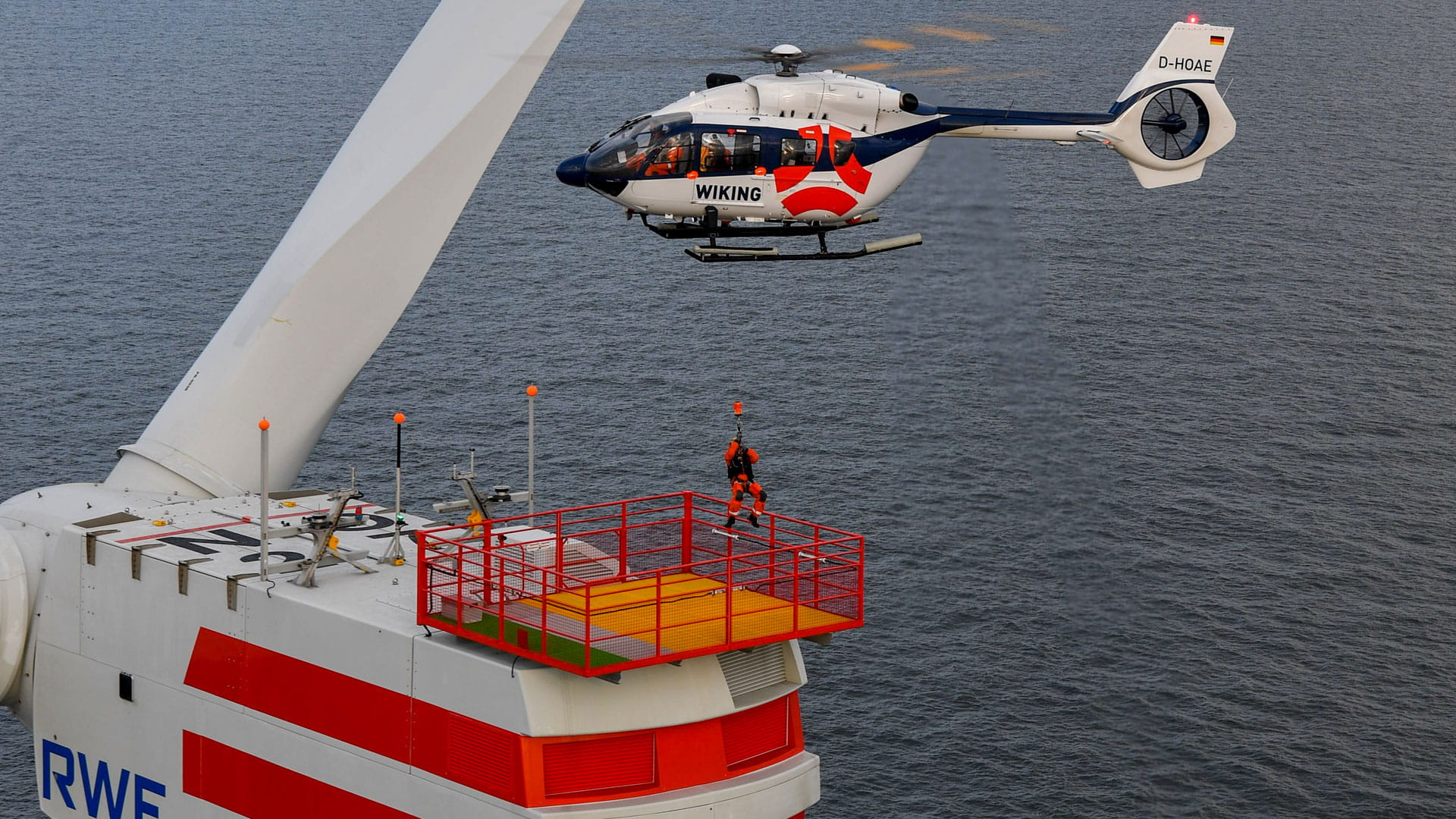 A helicopter lowers a man down to a platform using a hoist.