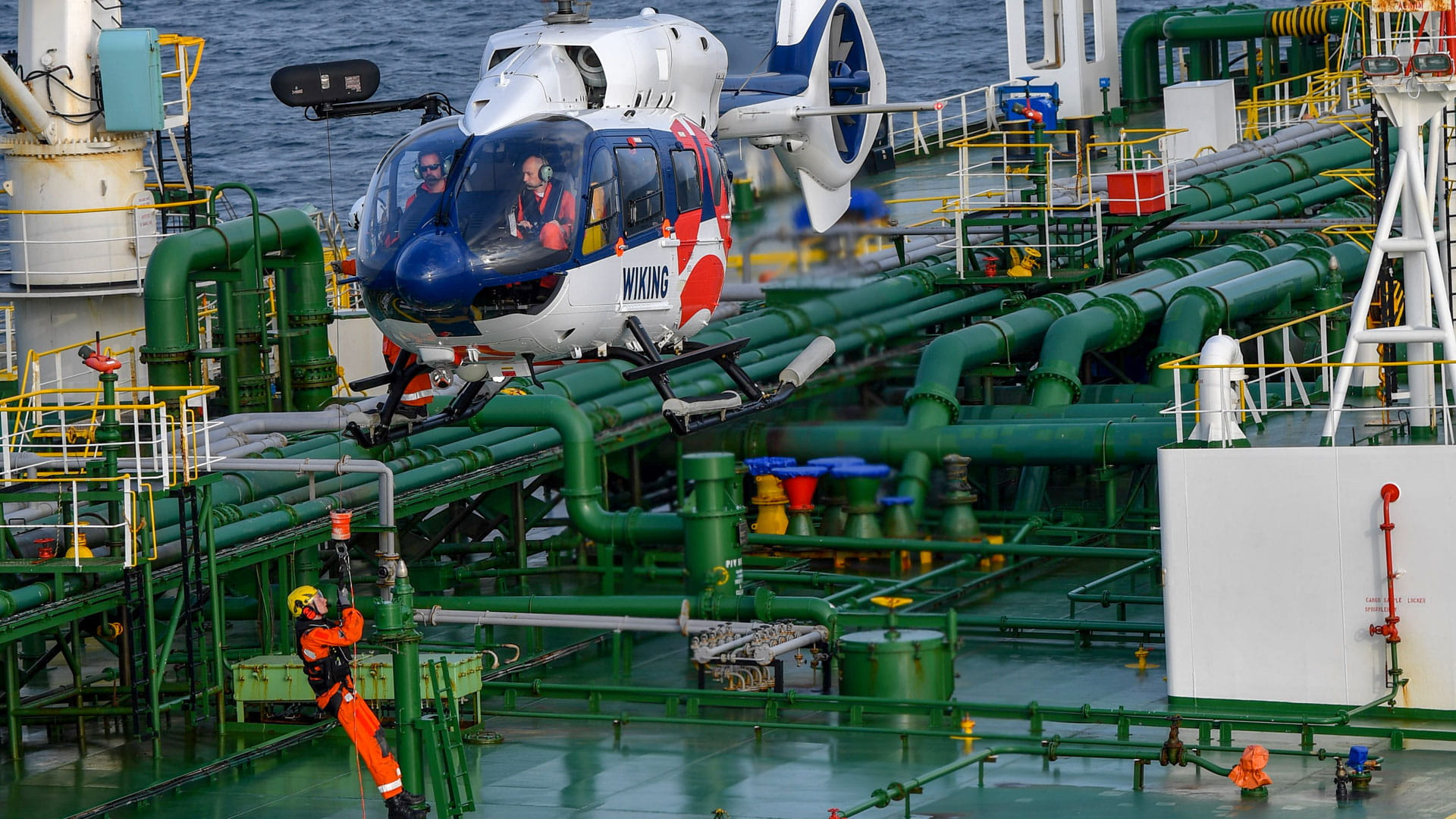 A helicopter lowers a man onto a ship via hoist