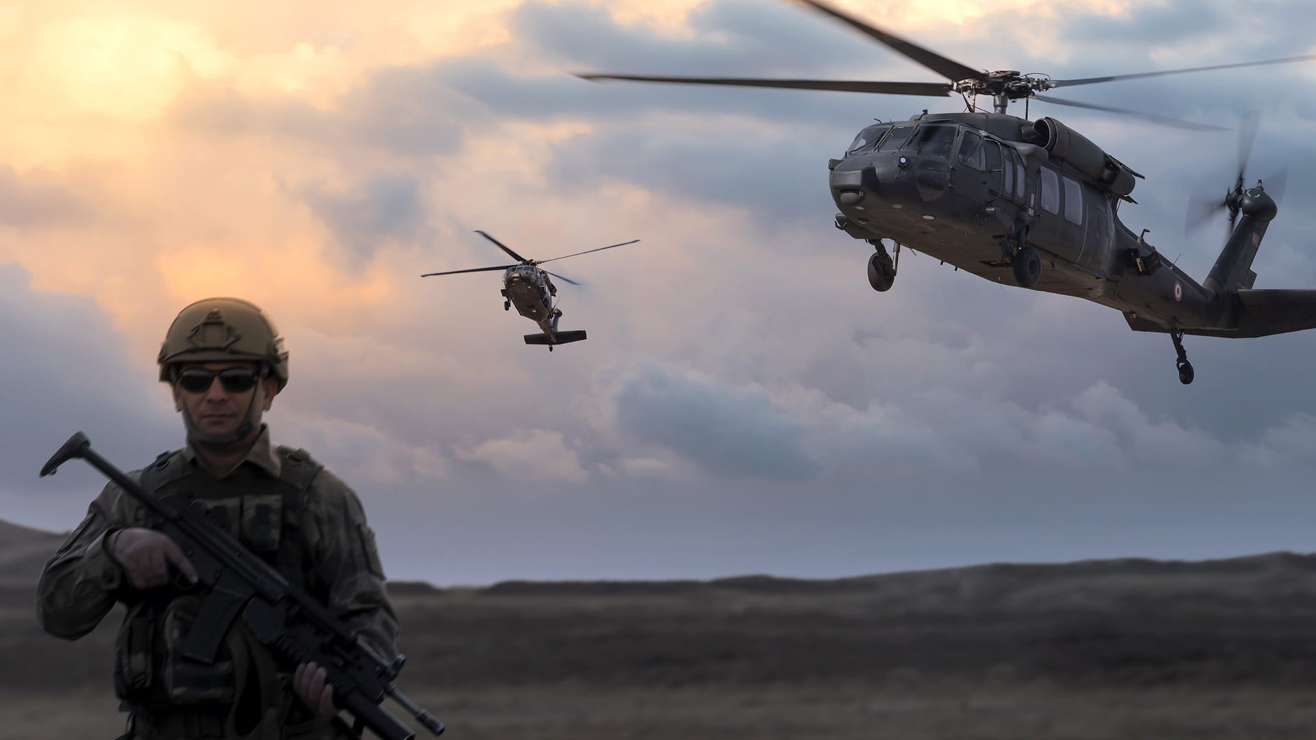 Soldier standing in a field with two helicopters in the background