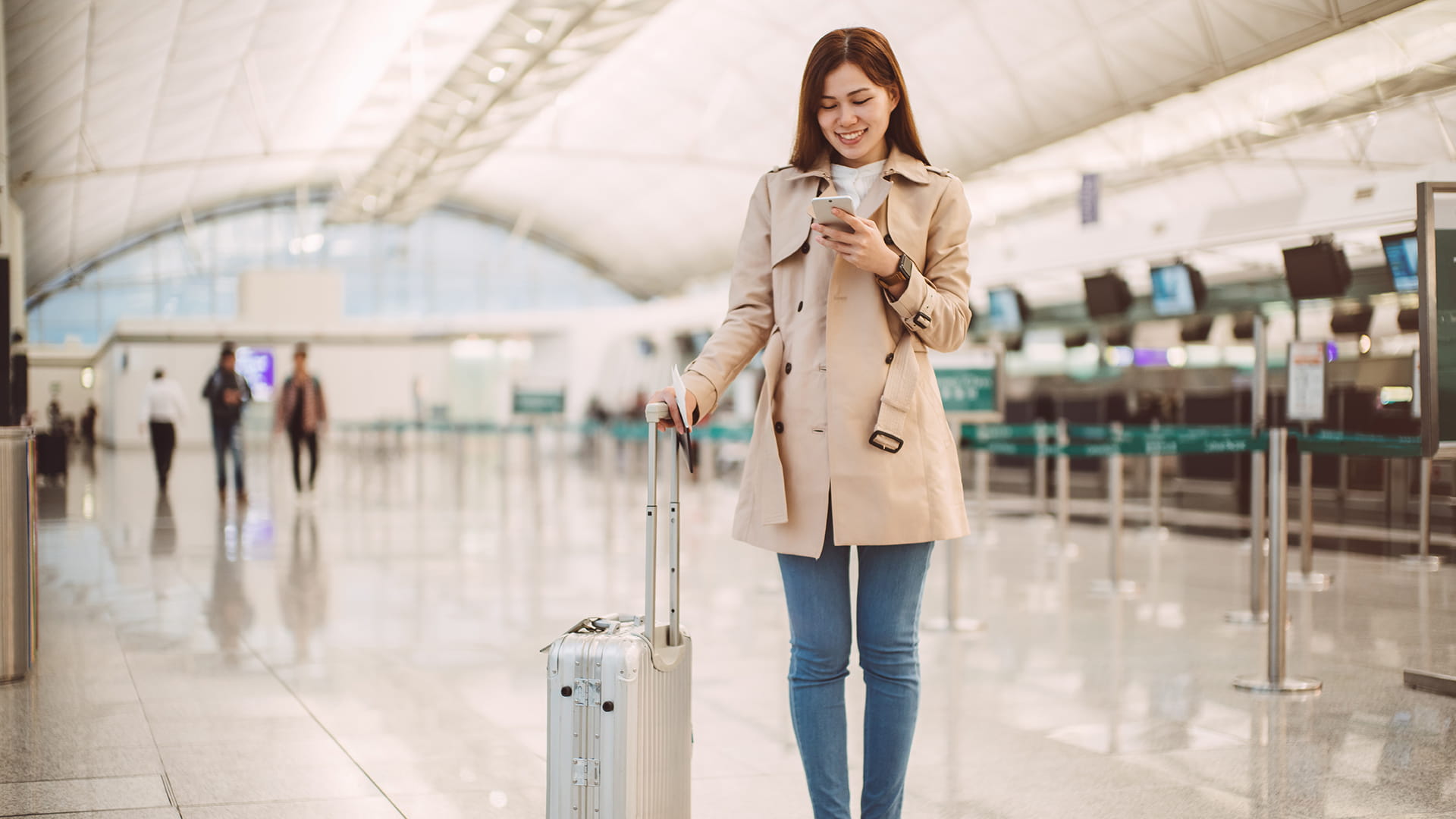 A smiling woman looks at her smartphone while in an airport.
