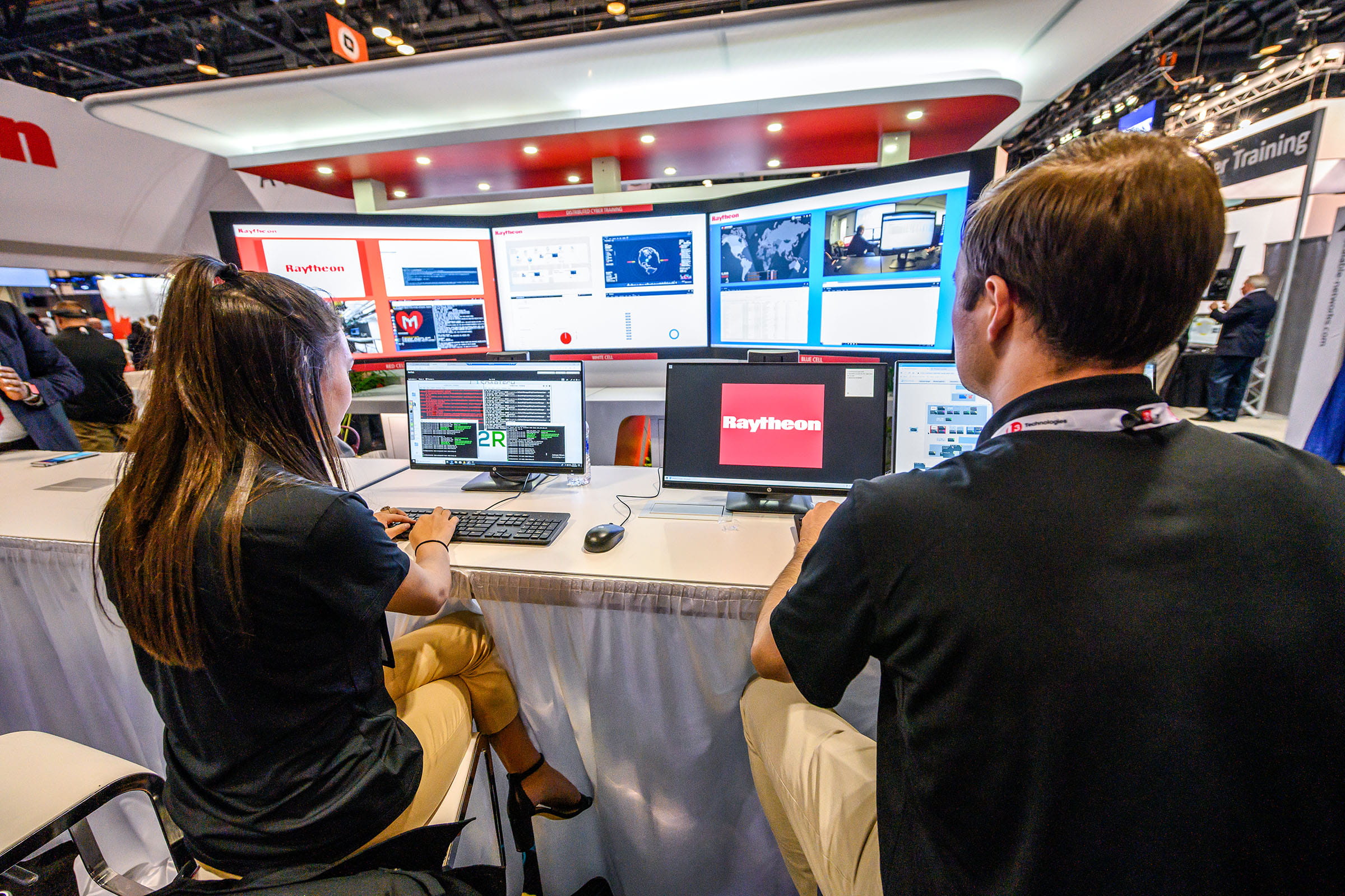 Pictured are two Raytheon Technologies employees presenting a demo of the company’s cyber training capabilities at an industry event.